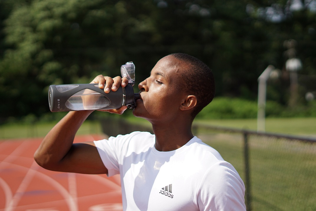 Man in white shirt drinking from black water bottle on track
